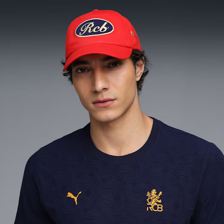 Close up of the premium gold embroidered RCB insignia on the front panel of the Puma IPL red baseball cap.
