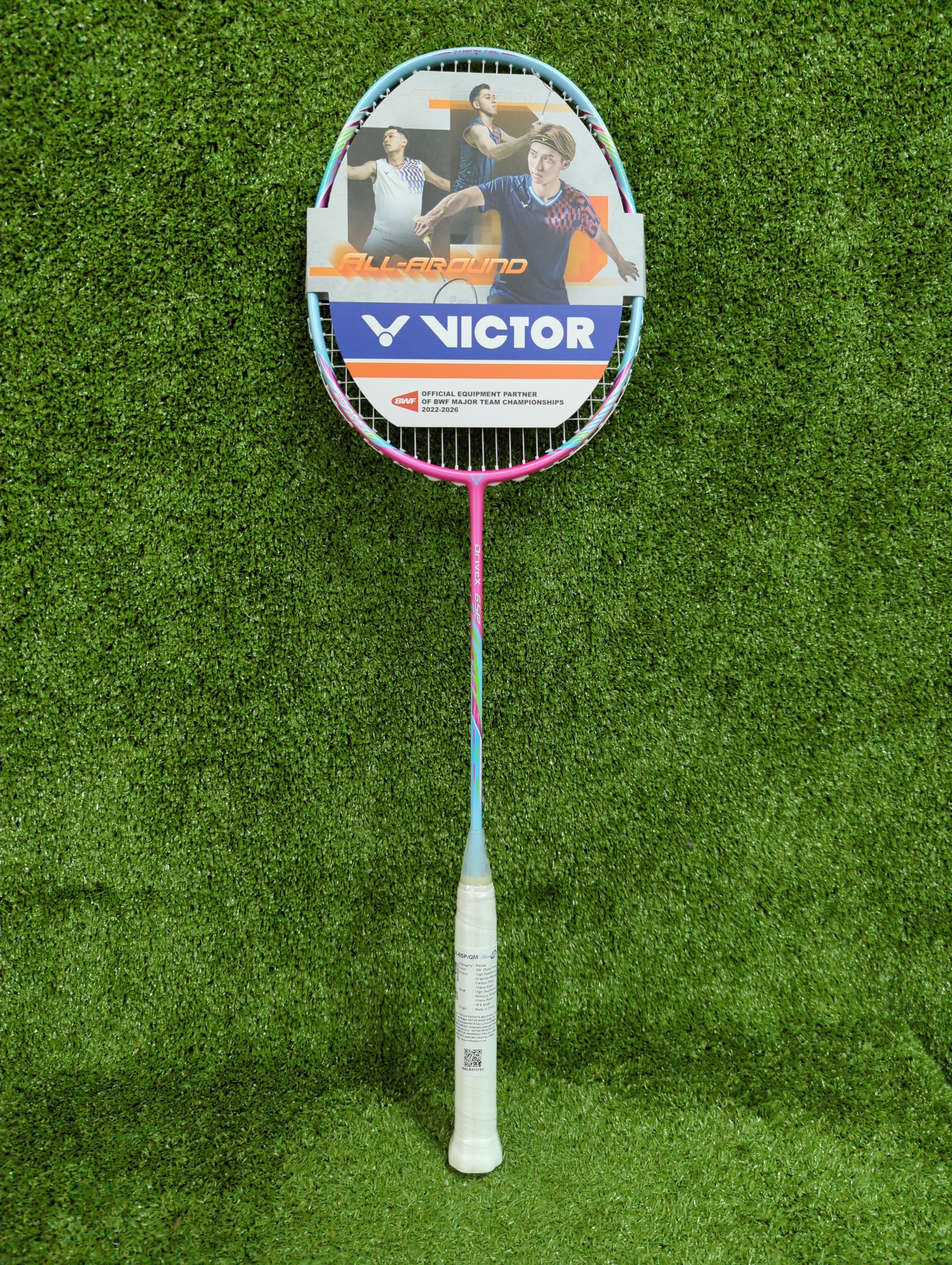 Victor DriveX 6SP QM badminton racket in pink and teal, full view on grass background.